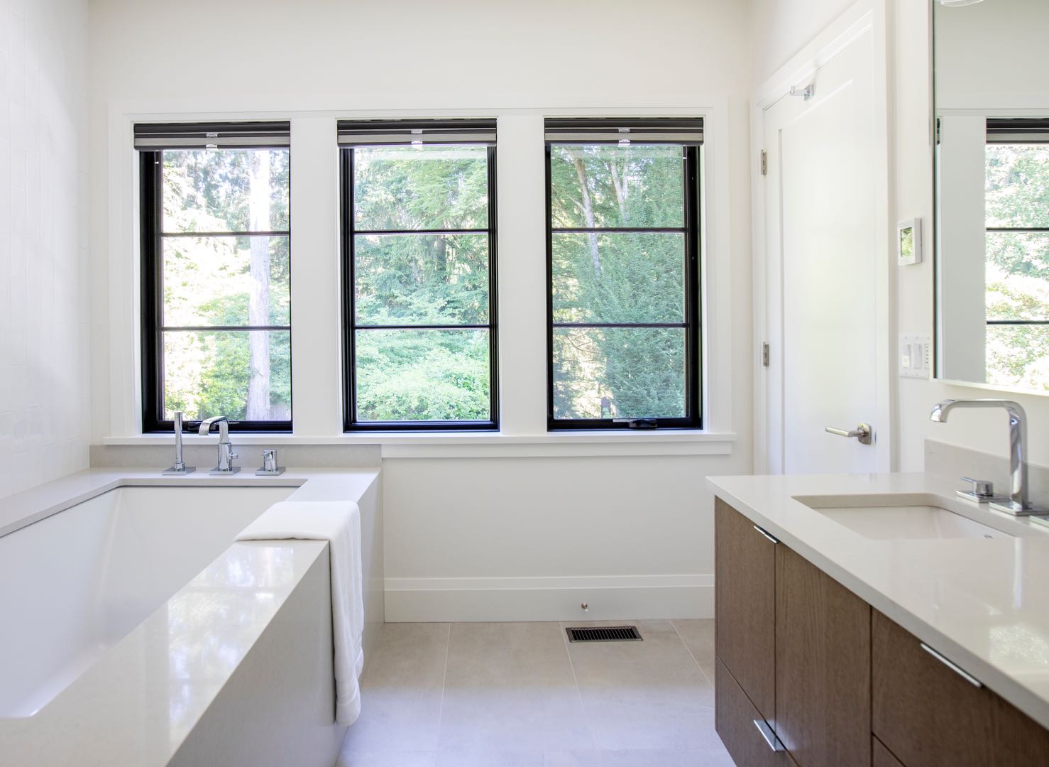 Light surfaces around the vanity and bathtub sit beside black-framed windows. The simple combination gives the room a calm, open feel.